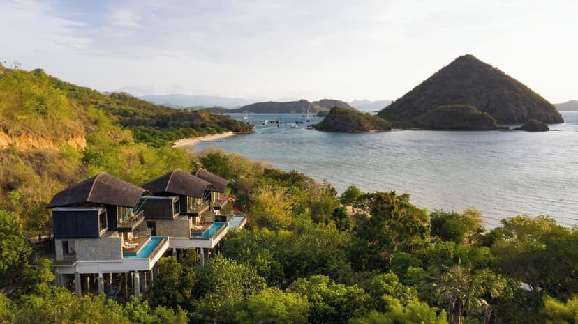 Hero/establishing shot of Plataran Komodo Resort & Spa, Labuan Bajo, Indonesia. An intimate Michelin-Key villa resort on Waecicu Beach, Labuan Bajo — named Best for Romance by Condé Nast Johansens — with villas on a leafy hillside facing th