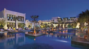 Hero/establishing shot of Sharq Village & Spa, a Ritz-Carlton Hotel, Doha, Qatar. A heritage Qatari village-style beach resort along the Doha coastline, with marbled Sheikh’s-palace design and a Michelin Key.