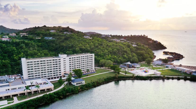 Hero/establishing shot of Royalton Antigua, Antigua. A big-brand Marriott Autograph Collection all-inclusive on calm Deep Bay below historic Fort Barrington, with a genuine Caribbean rarity — six over-water bungalows with glass floors and s