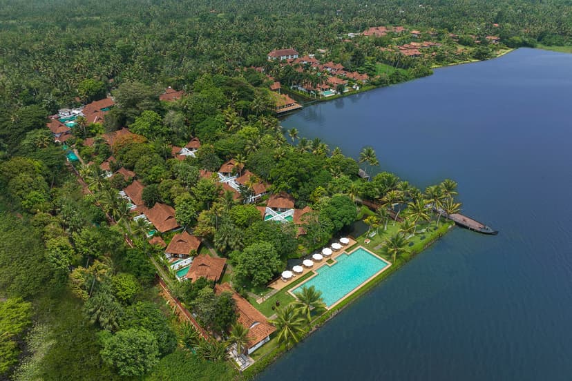 Hero/establishing shot of Kumarakom Lake Resort (Kerala), Kerala, India. A heritage backwater resort on Lake Vembanad in Kerala, where villas are reconstructed 16th-century Kerala ‘manas’ — relocated and reassembled — surrounded by paddy fi