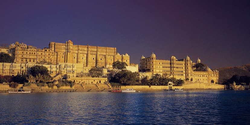 Hero/establishing shot of The Oberoi Udaivilas, Udaipur, Udaipur, India. A grand lake-palace on the banks of Lake Pichola in Udaipur, the City of Lakes — 30 acres of Mewar-inspired domes and gardens facing the City Palace, reached by a priv