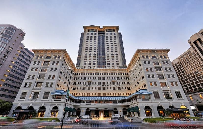 Hero/establishing shot of The Peninsula Hong Kong, Hong Kong. The Grande Dame of the Far East — a 1928 heritage icon on Victoria Harbour in Tsim Sha Tsui, with a fleet of Peninsula-green Rolls-Royces, a rooftop helipad and a yacht.